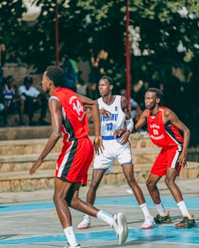 Three basketball players in action on an outdoor court during a daytime game.